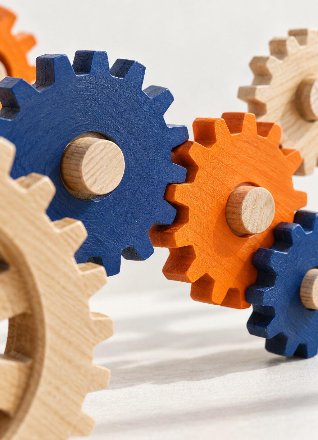 Wooden gears in blue, orange and natural wood interlocking, close up against a light background.