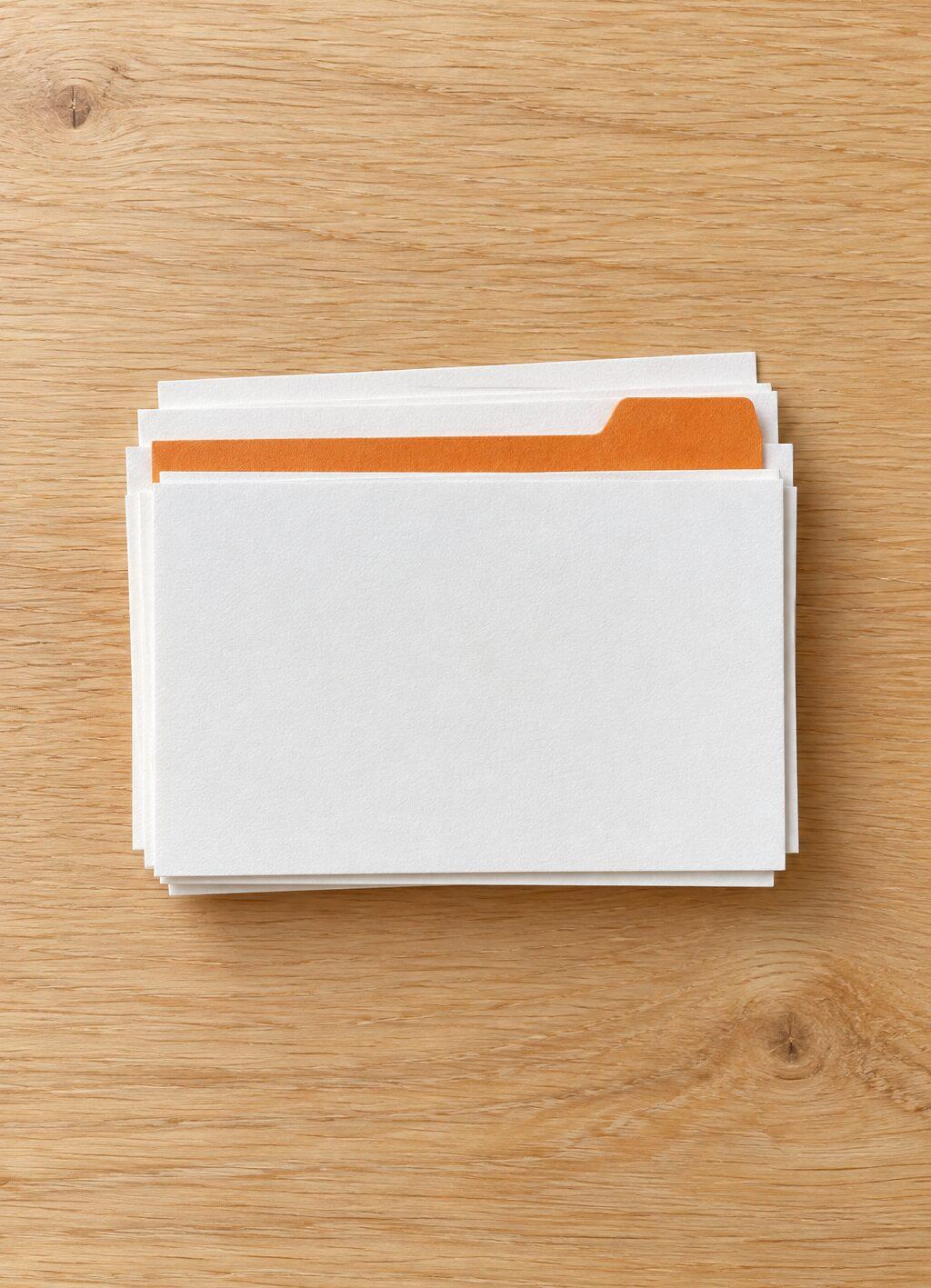 Een stapel blanco kaartjes met een enkele oranje tabkaart ertussen, van bovenaf op een houten bureau.