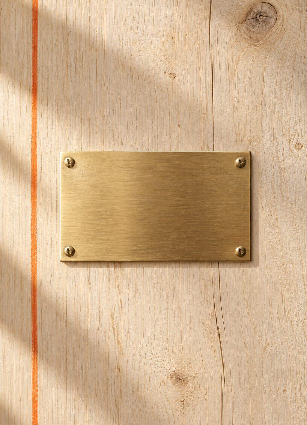 A blank brushed brass nameplate on a light wooden facade panel in warm side light