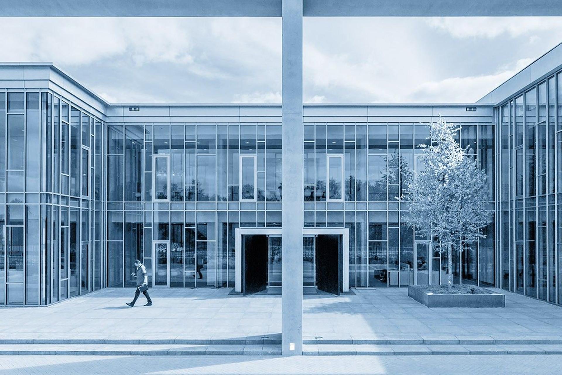 JM van Delft & zn: blauwgetint beeld van een modern kantoorpand met glazen gevel en een voorbijganger.